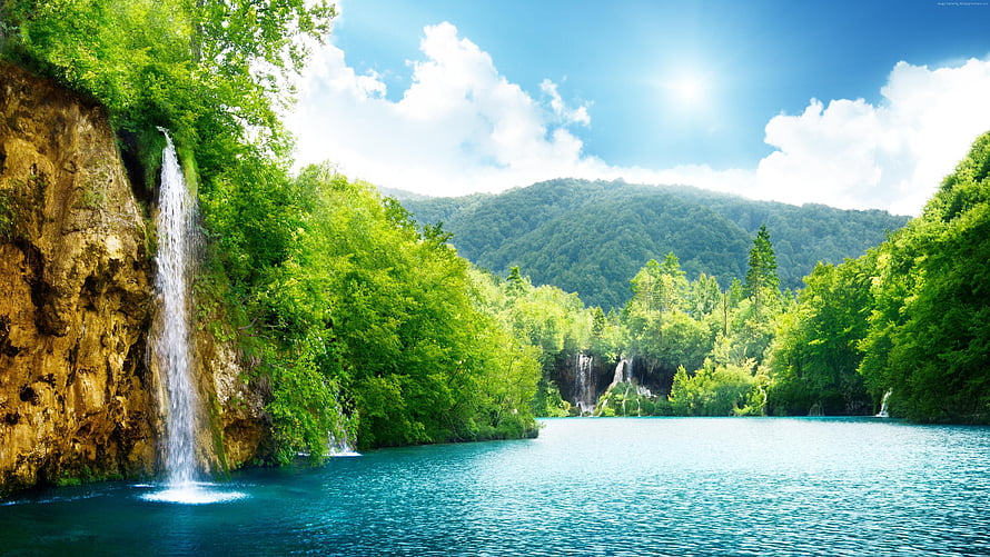 Serene turquoise lake surrounded by lush green forest and cascading waterfalls under a bright blue sky HD wallpaper