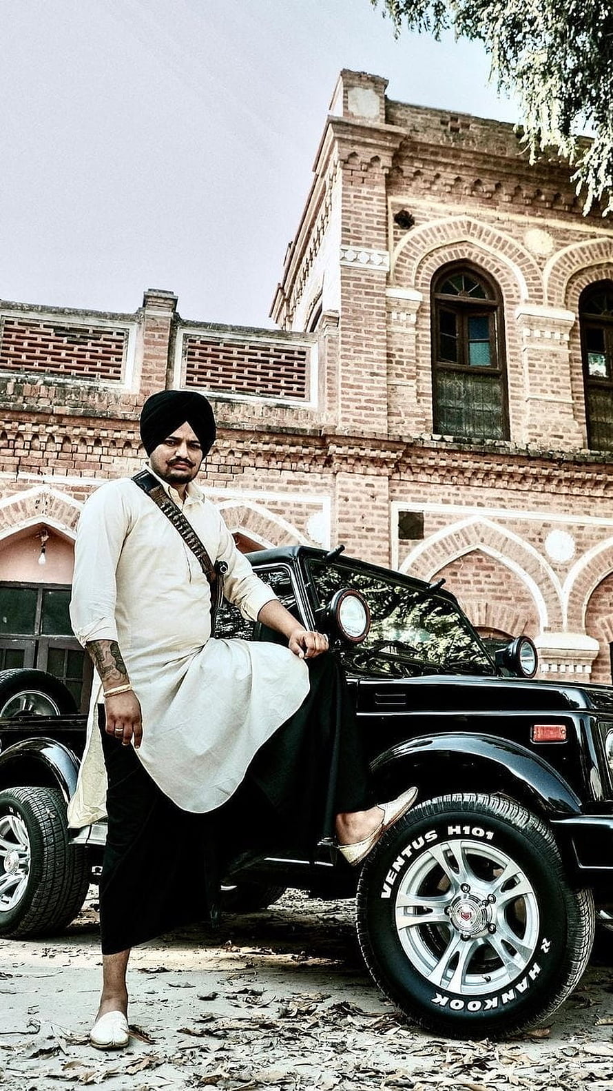 Sikh man in traditional attire posing with a black SUV in front of a historic brick building, Sidhu Moose Wala, Black Jeep, Background HD phone wallpaper