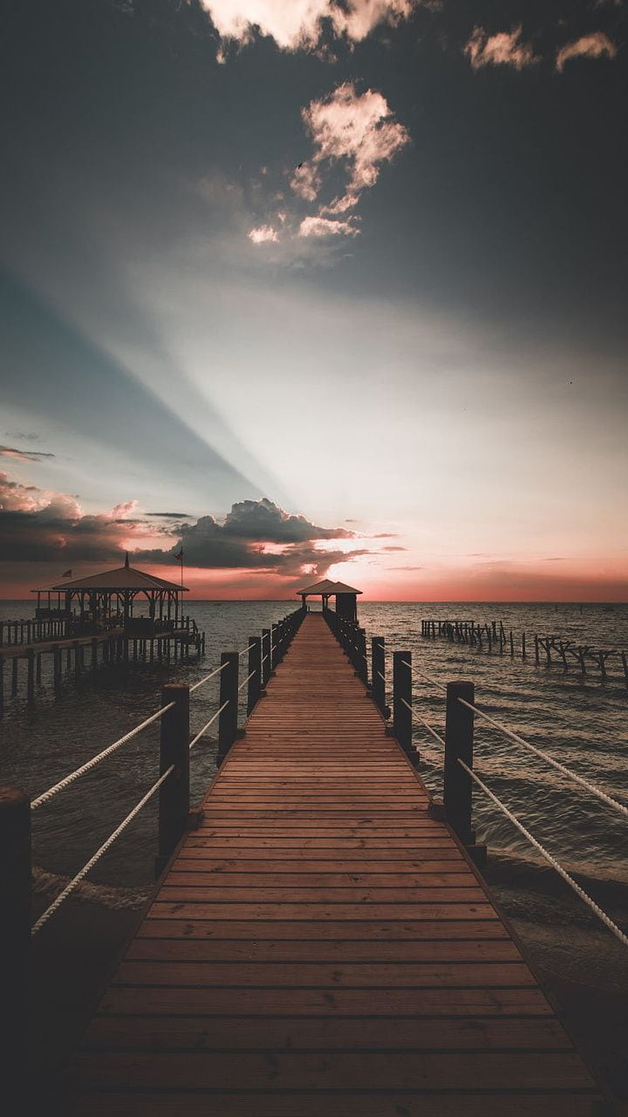 Serene Wooden Pier Leading to Ocean Sunset with Dramatic Clouds and Light Rays HD phone wallpaper