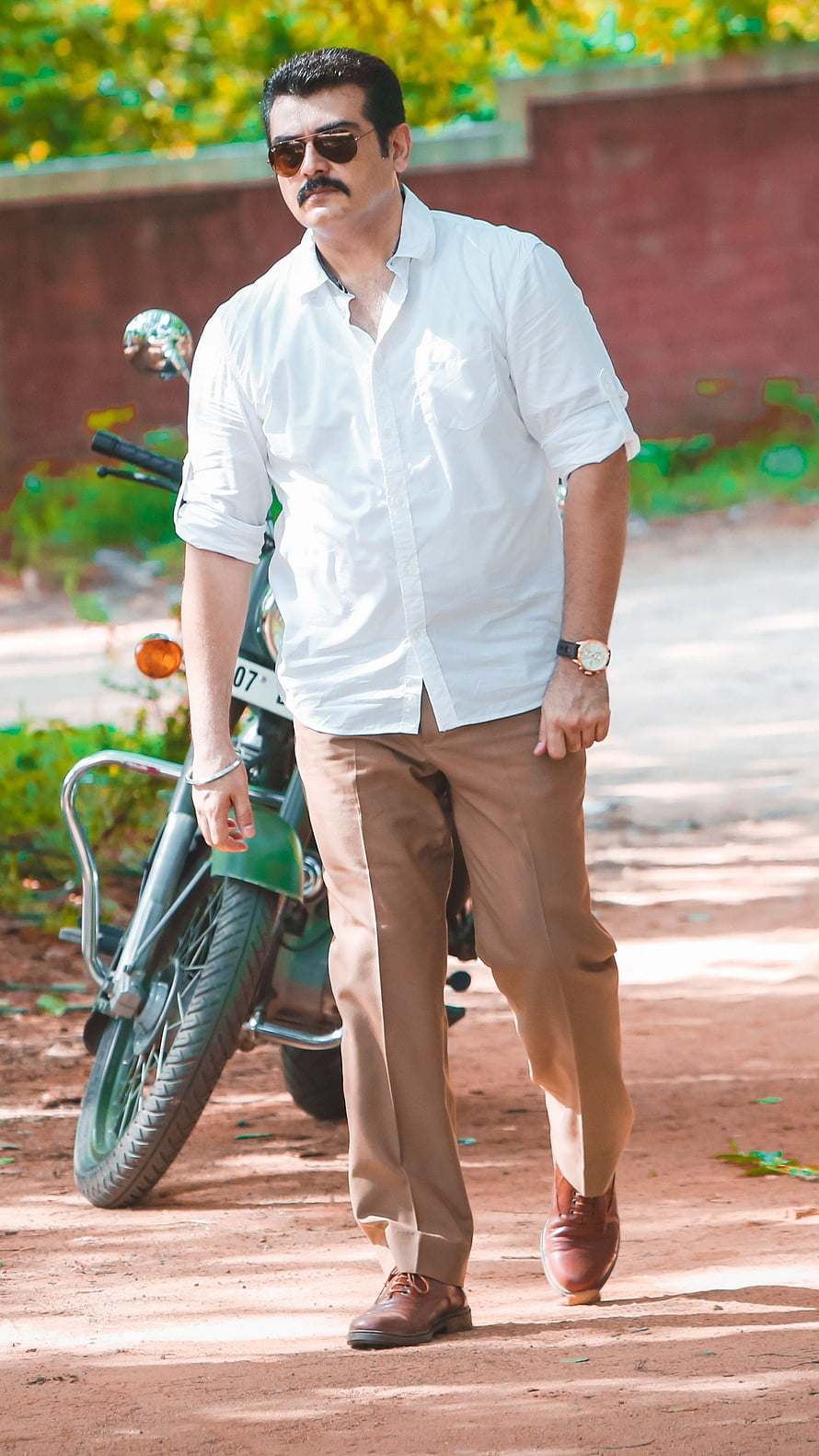 Ajith Kumar in White Shirt and Sunglasses Walking Past a Green Motorcycle HD phone wallpaper