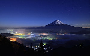 Mount Fuji at Night with Starry Sky and City Lights Below a Sea of Clouds HD wallpaper