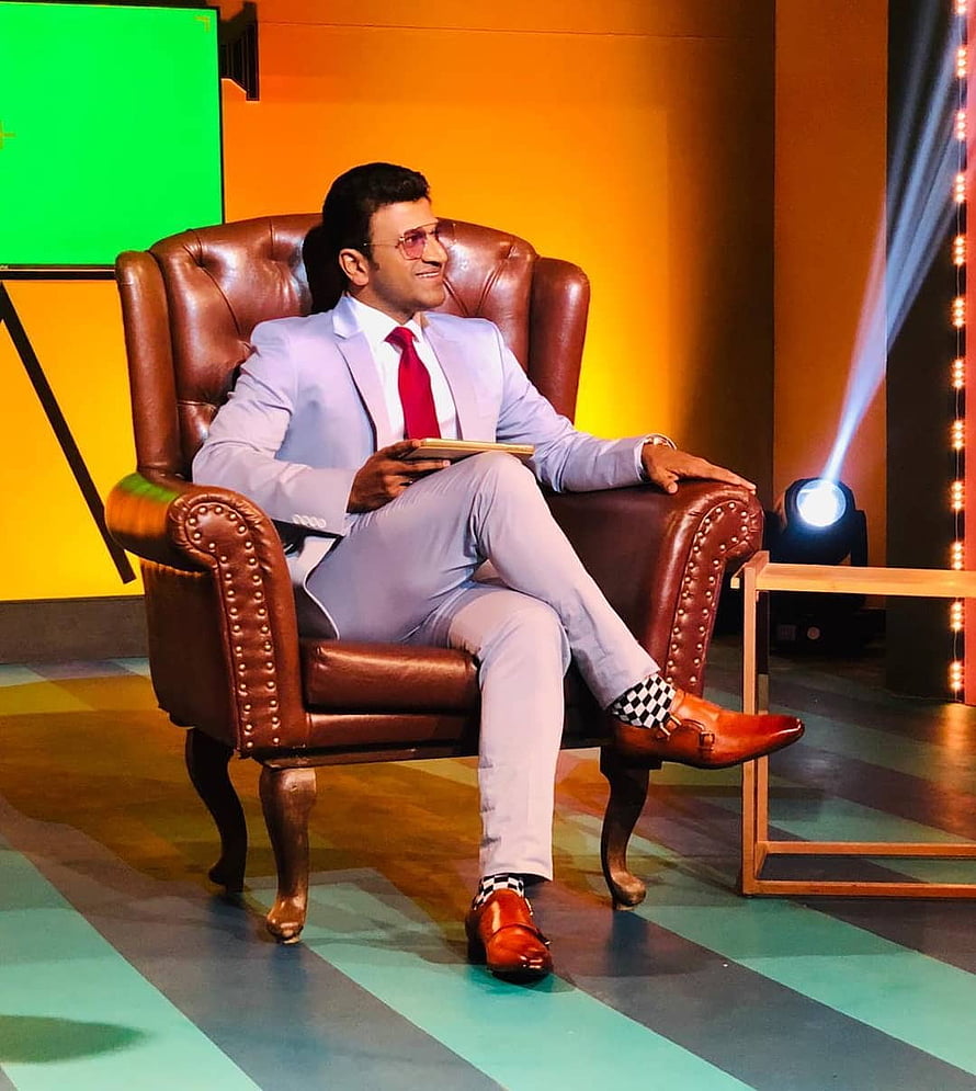 Puneeth Rajkumar in Light Grey Suit and Red Tie Seated in Brown Leather Armchair on Stage HD phone wallpaper