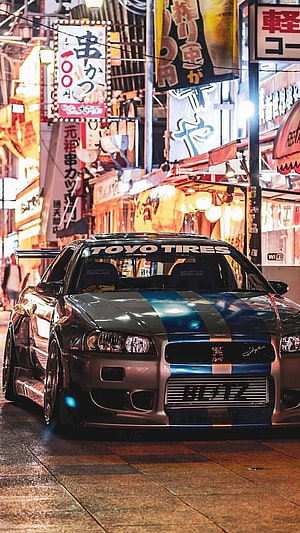 Nissan Skyline GT-R R34 in Japanese Street Scene with Neon Signs HD phone wallpaper