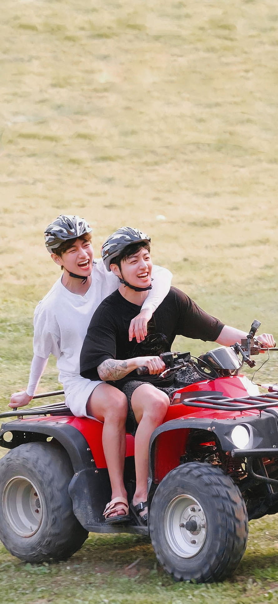 BTS V and Jungkook riding a red ATV in a grassy field wearing helmets HD phone wallpaper
