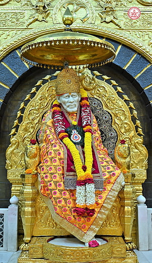 Golden Statue of Sai Baba Seated on Ornate Throne with Flower Garlands HD phone wallpaper