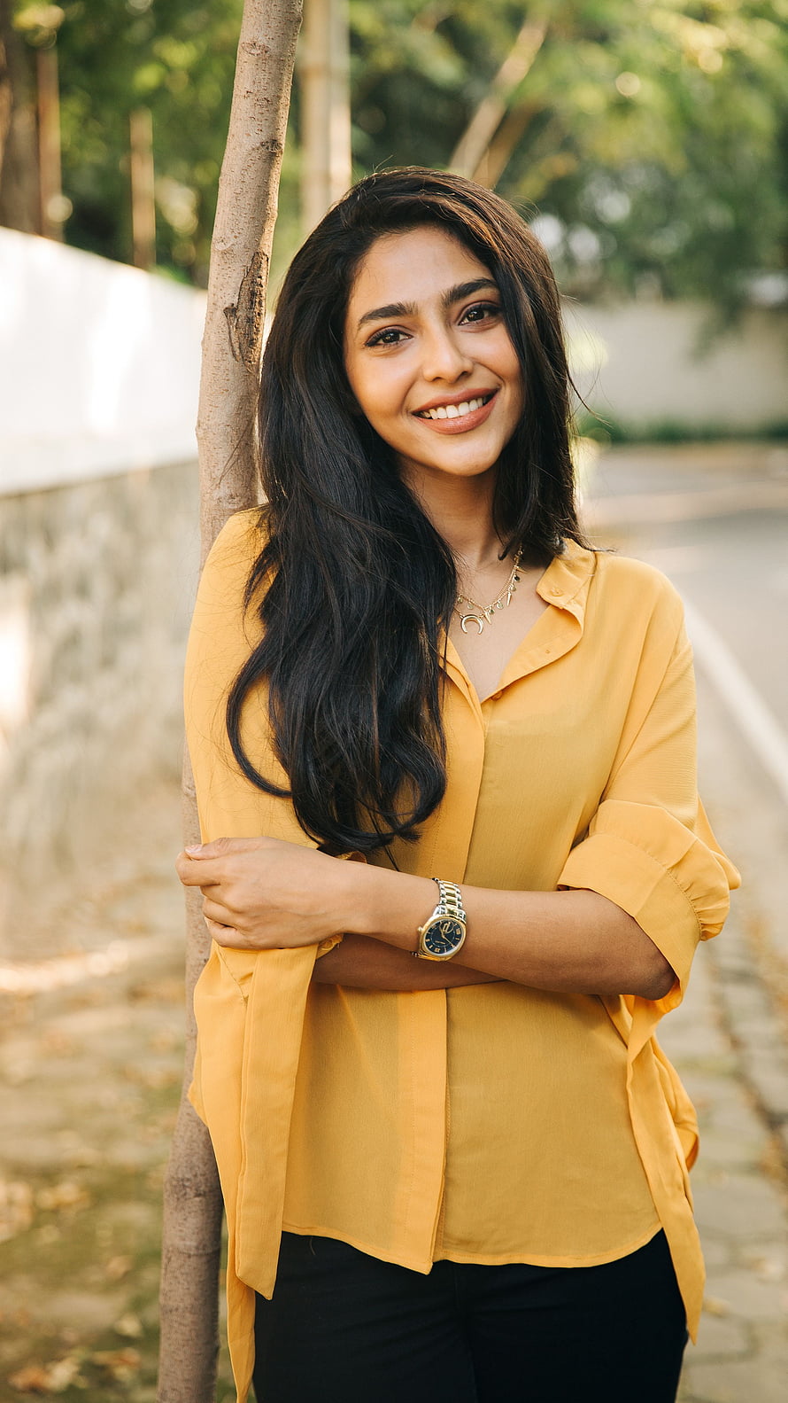 Aishwarya Lekshmi in a mustard yellow shirt leaning against a tree outdoors HD phone wallpaper