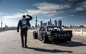 Ken Block and the Hoonicorn drag car on a bridge with a city skyline in the background HD wallpaper
