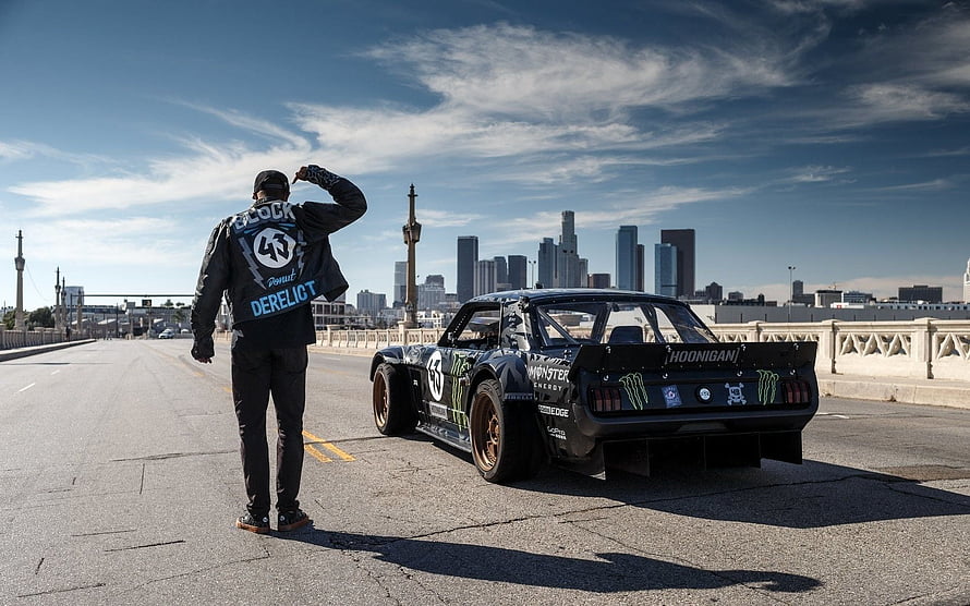Ken Block and the Hoonicorn drag car on a bridge with a city skyline in the background HD wallpaper