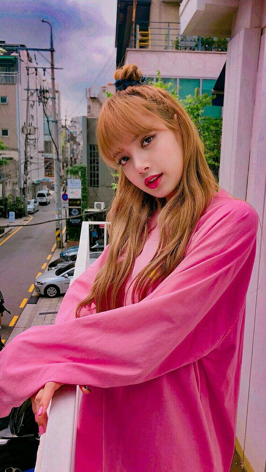 Lisa Blackpink in a pink velvet top on a city balcony with long blonde hair and a top bun HD phone wallpaper