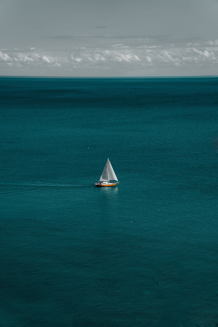 Lone Sailboat Drifting on Vast Teal Ocean Under Overcast Sky HD phone wallpaper