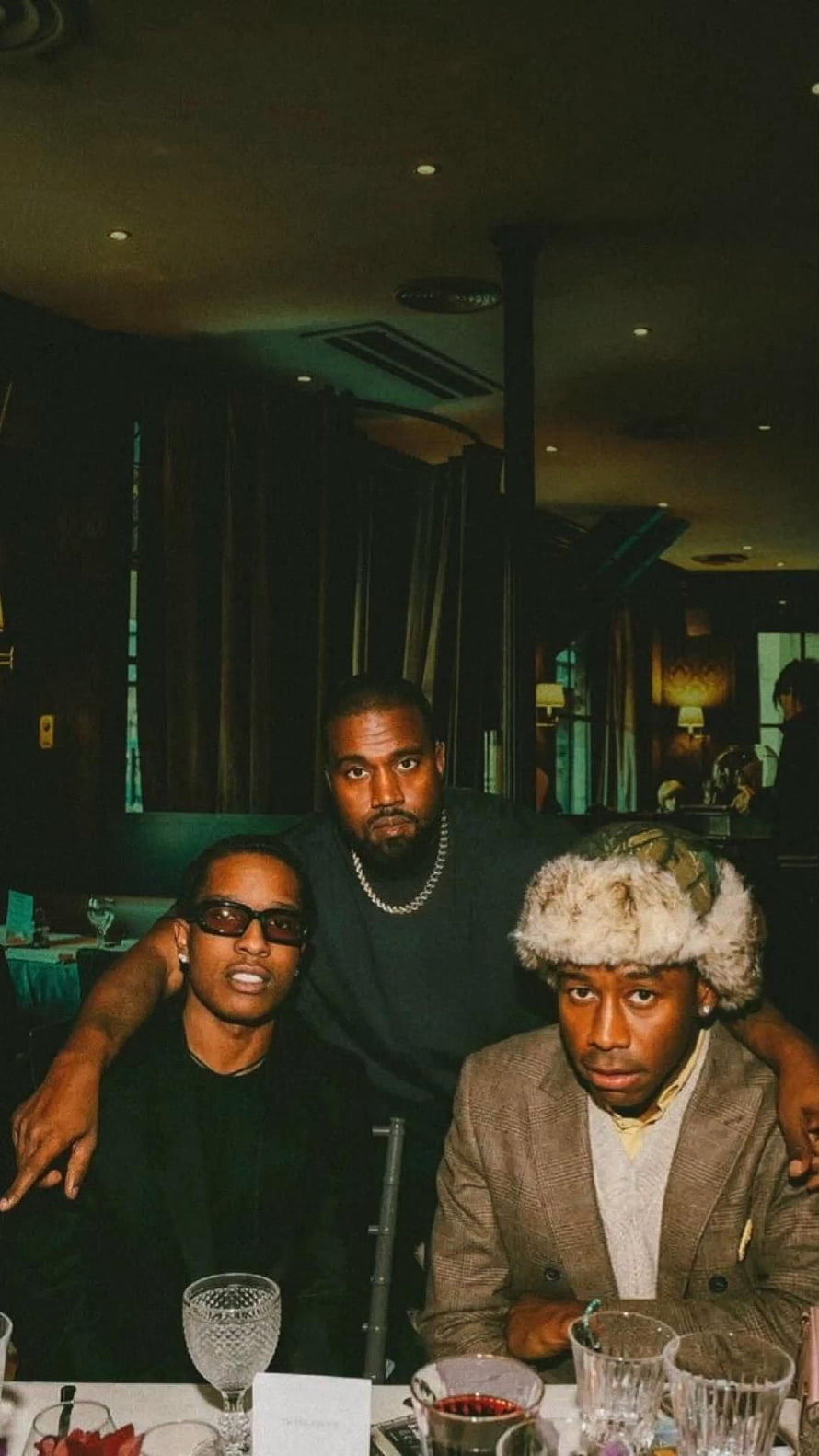 Kanye West, A$AP Rocky, and Tyler, the Creator at a dimly lit restaurant table HD phone wallpaper