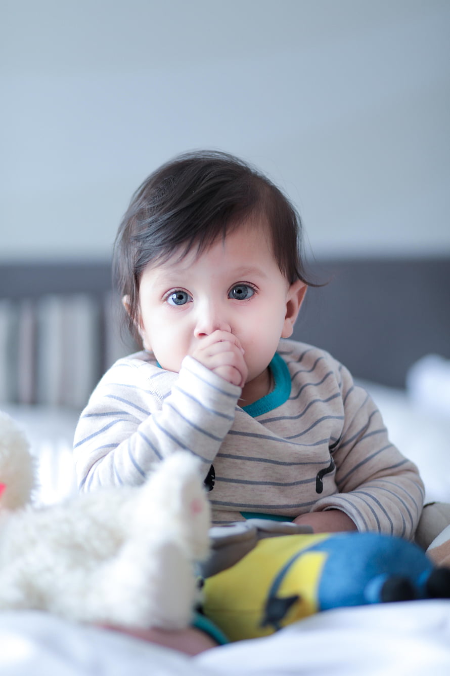 Cute Baby With Blue Eyes Sucking Thumb On Bed With Stuffed Toys HD phone wallpaper