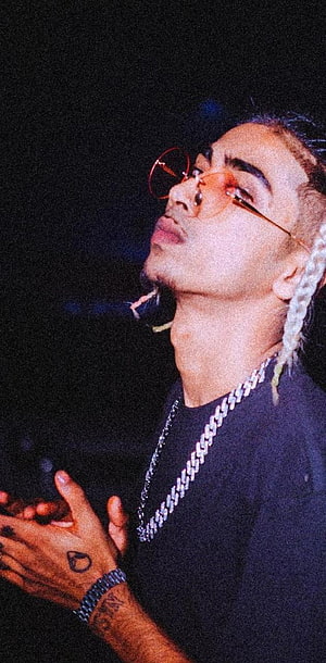 Young man with braided hair, orange glasses, and a silver chain necklace against a dark background, Mc stan HD phone wallpaper
