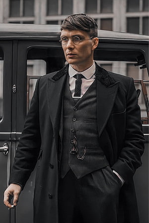 Thomas Shelby in a dark three-piece suit and round glasses standing beside a vintage car HD phone wallpaper