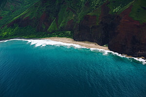Aerial View of Turquoise Ocean Waves Crashing Against a Secluded Sandy Beach and Lush Green Cliffs HD wallpaper