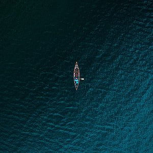 Aerial View of a Solitary Canoe Drifting on Deep Teal Ocean Waters HD phone wallpaper