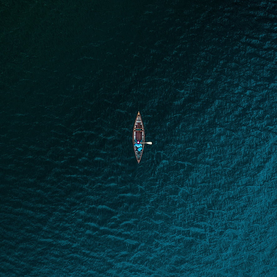 Aerial View of a Solitary Canoe Drifting on Deep Teal Ocean Waters HD phone wallpaper