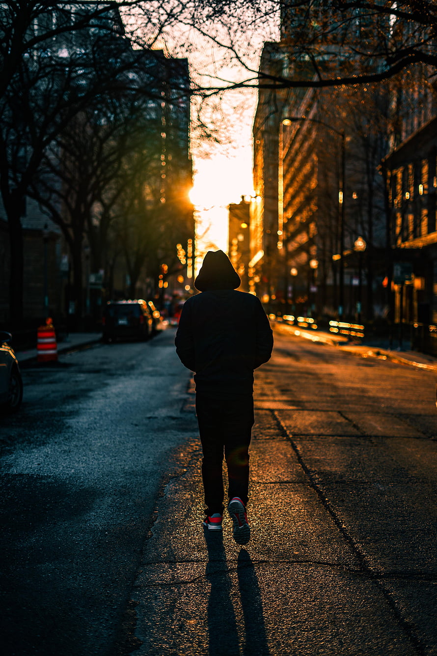 Silhouette of a person in a hood walking down a city street at golden hour HD phone wallpaper