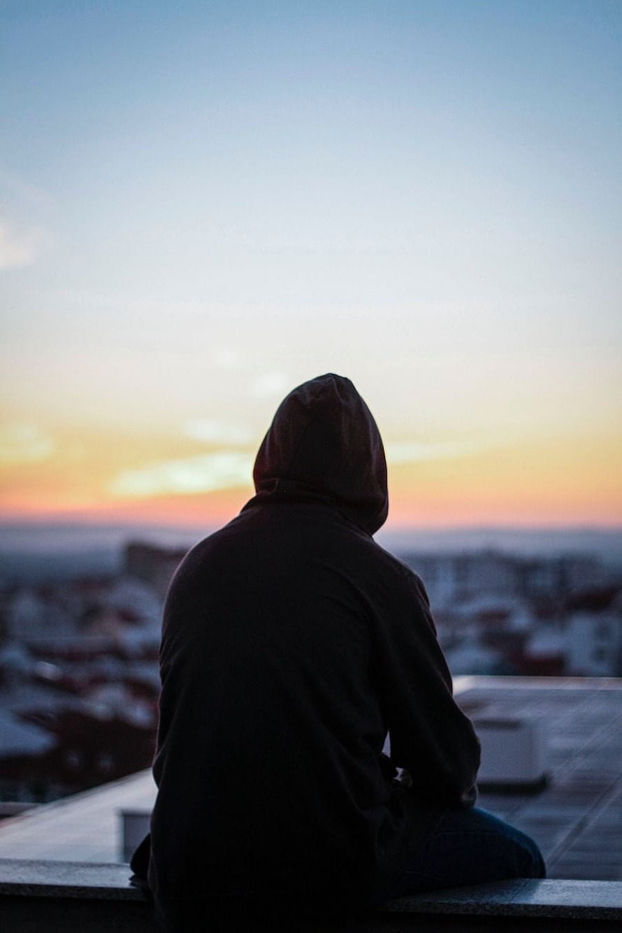 Silhouette of a Hooded Figure Sitting on a Rooftop Watching a Colorful Sunset Over the City HD phone wallpaper