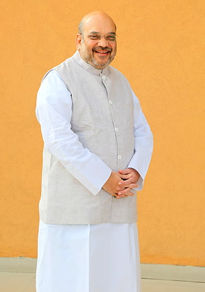 Amit Shah in traditional white kurta and grey Nehru jacket against a warm ochre wall HD phone wallpaper