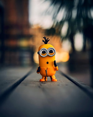 Cute Minion Figurine Standing on Wooden Planks with Bokeh Background HD phone wallpaper