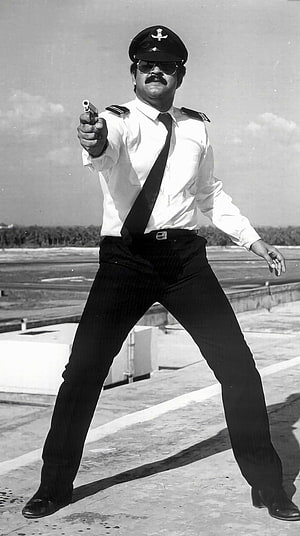 Mohanlal in a dramatic police officer pose holding a pistol on a rooftop HD phone wallpaper