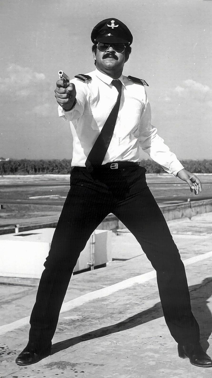Mohanlal in a dramatic police officer pose holding a pistol on a rooftop HD phone wallpaper