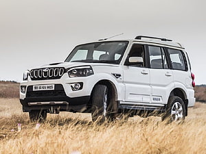 White Mahindra Scorpio SUV parked in a dry grassy field under an overcast sky HD wallpaper