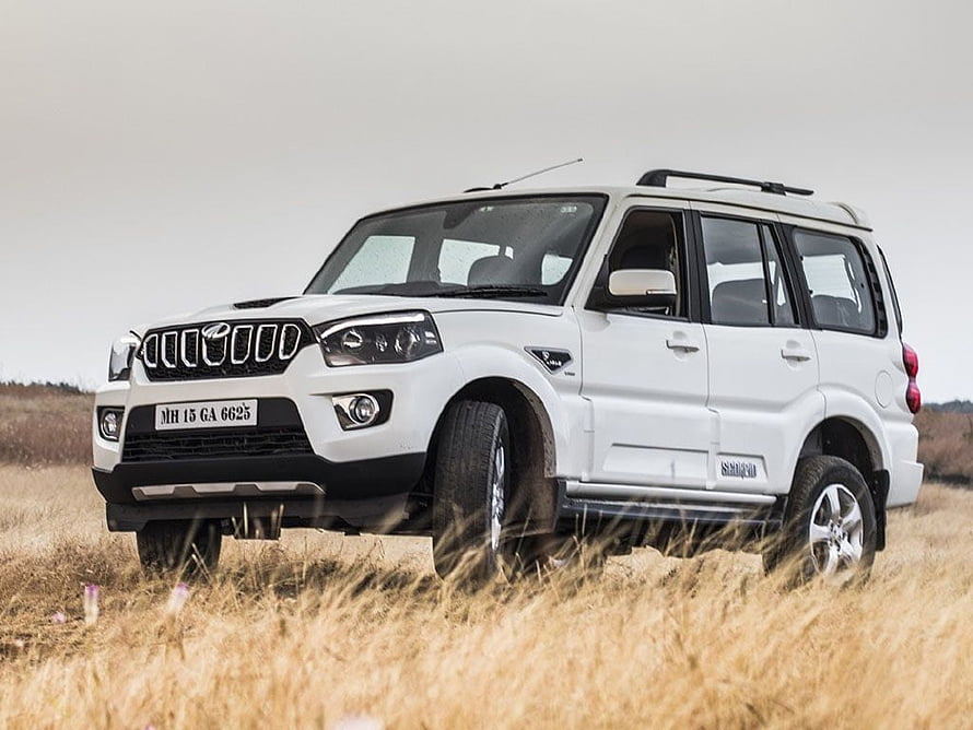 White Mahindra Scorpio SUV parked in a dry grassy field under an overcast sky HD wallpaper