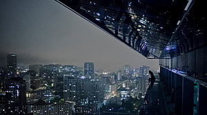 Silhouette of a person sitting on a high-rise ledge overlooking a sprawling city skyline at night HD wallpaper