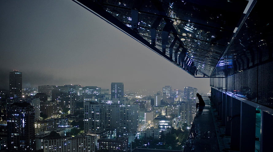 Silhouette of a person sitting on a high-rise ledge overlooking a sprawling city skyline at night HD wallpaper