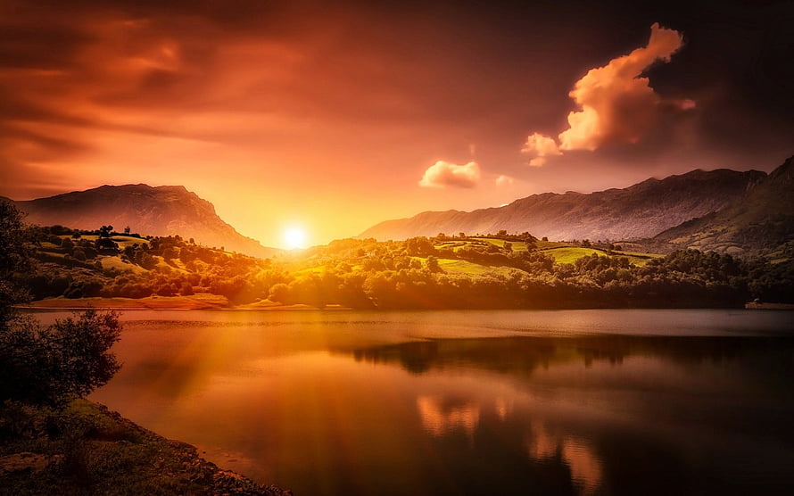 Golden sunset over a calm mountain lake with dramatic clouds and rolling hills HD wallpaper