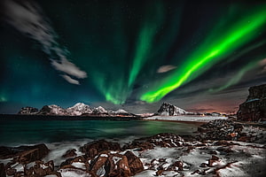 Vibrant Green Aurora Borealis Dancing Over Snowy Arctic Mountains and Coastal Rocks HD wallpaper