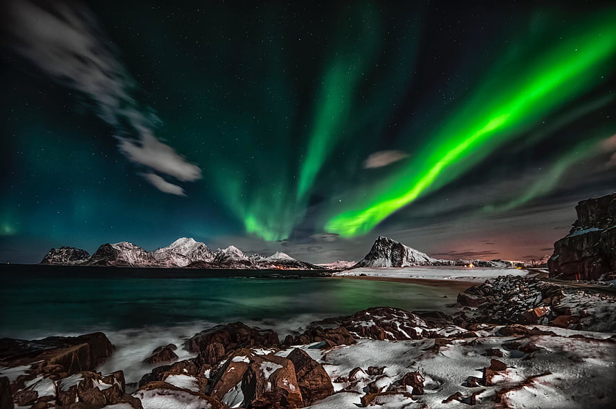 Vibrant Green Aurora Borealis Dancing Over Snowy Arctic Mountains and Coastal Rocks HD wallpaper