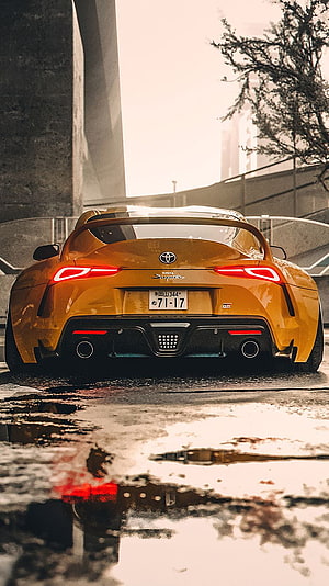 Rear View of a Golden Toyota Supra Parked on Wet Urban Street with Reflections HD phone wallpaper