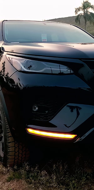 Close-up of a black SUV front corner with glowing amber turn signal and rugged tire HD phone wallpaper
