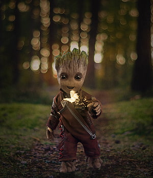 Baby Groot from Guardians of the Galaxy holding a glowing butterfly in a magical forest HD phone wallpaper