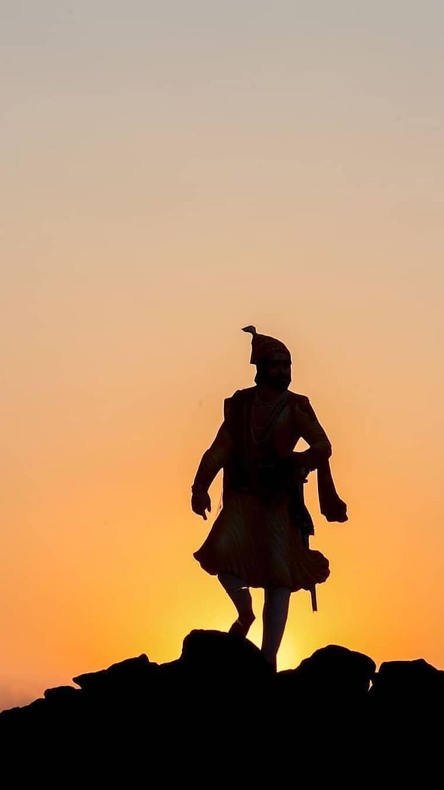 Silhouette of a historical warrior statue standing on a rocky peak against a vibrant orange sunset sky HD phone wallpaper