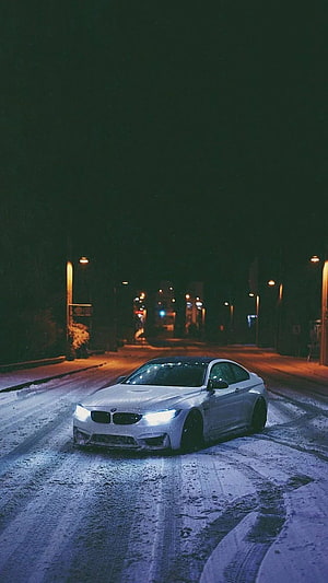White BMW M4 Coupe Driving on Snowy Street at Night with Headlights On HD phone wallpaper