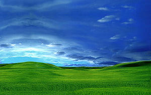 Rolling Green Hills Under a Dramatic Blue Sky with Scattered Clouds HD wallpaper