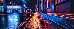 Neon-lit wet city street at night with vibrant red and blue reflections on the pavement HD wallpaper