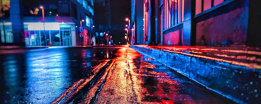 Neon-lit wet city street at night with vibrant red and blue reflections on the pavement HD wallpaper