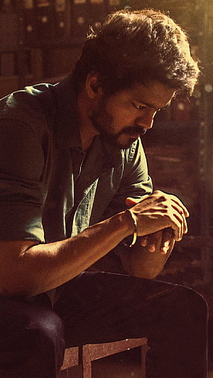 Vijay in a contemplative seated pose with warm cinematic lighting and a moody atmosphere HD phone wallpaper