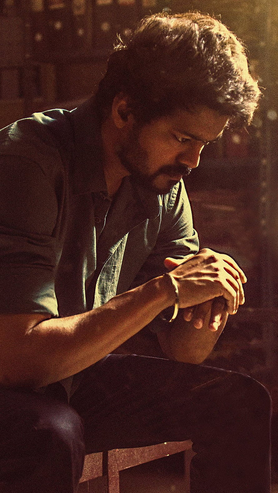 Vijay in a contemplative seated pose with warm cinematic lighting and a moody atmosphere HD phone wallpaper
