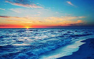 Serene Ocean Sunset With Vibrant Orange Sky And Gentle Blue Waves Rolling Onto Sandy Shore HD wallpaper
