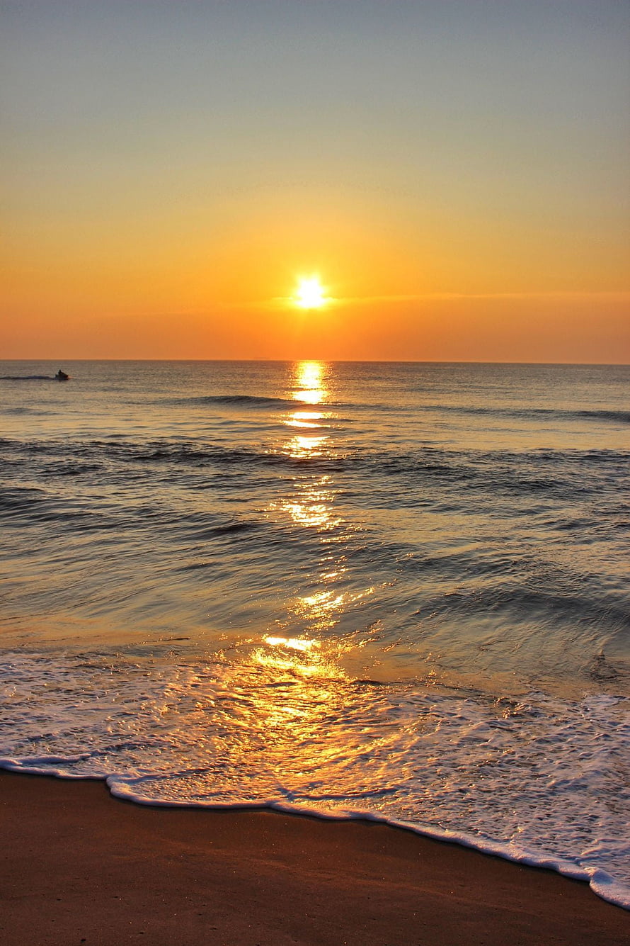 Golden sunrise over calm ocean waves with a distant boat on the horizon HD phone wallpaper