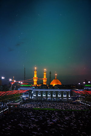 Night view of Imam Reza shrine in Mashhad with golden dome and minarets illuminated above a vast crowd of worshippers HD phone wallpaper