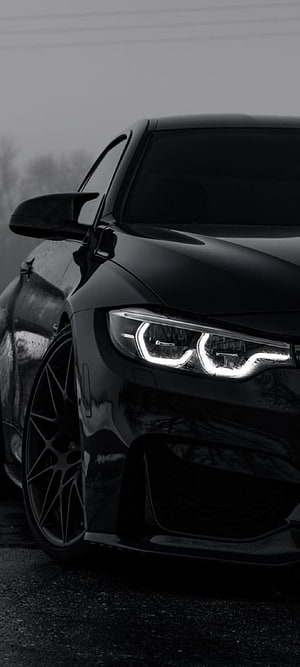Close-up of a black BMW M4 with illuminated angel eye headlights and custom wheels HD phone wallpaper