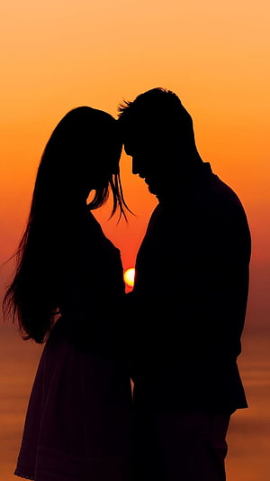 Romantic couple silhouette embracing against a warm orange sunset sky HD phone wallpaper