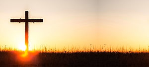 Silhouette of a wooden cross in a field at sunset with warm golden light HD wallpaper